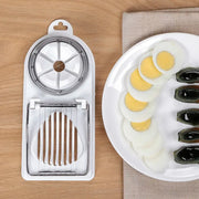 Multifunctional steel egg slicer with dual cutting tools and sliced eggs on a plate.