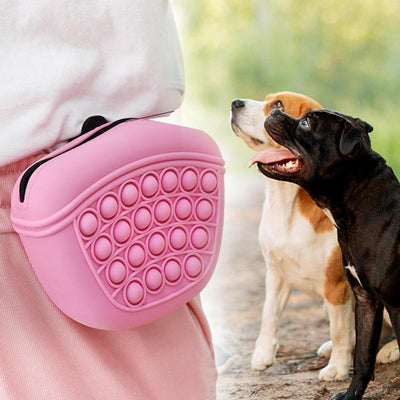 Silicone dog treat pouch attached to waist, used for pet training, in pink color near two dogs.